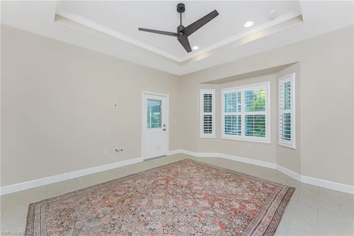 Tiled empty room with a tray ceiling, a wealth of natural light, and ornamental molding