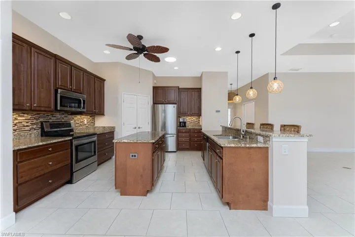 Kitchen featuring pendant lighting, sink, stainless steel appliances, light stone countertops, and a center island with sink