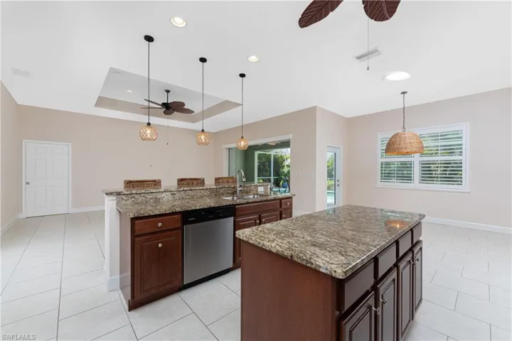 Kitchen featuring sink, dishwasher, a kitchen island with sink, a tray ceiling, and stone countertops