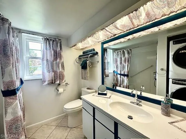 Bathroom with tile patterned flooring, a shower with shower curtain, vanity, stacked washer and dryer, and toilet