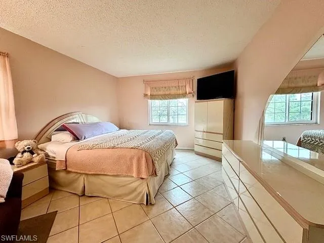 Tiled bedroom with a textured ceiling and multiple windows