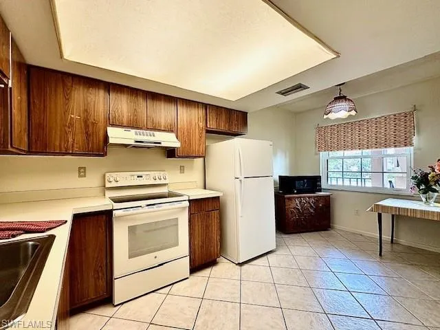 Kitchen featuring white appliances, decorative light fixtures, and light tile patterned floors