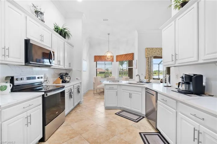 Kitchen with stainless steel appliances, tasteful backsplash, white cabinets, decorative light fixtures, and crown molding