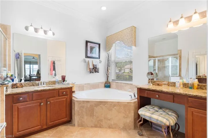 Bathroom with a shower stall, a garden tub, crown molding, two vanities, and light tile patterned floors
