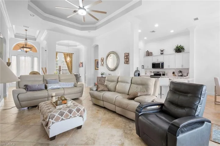 Living area with a high ceiling, crown molding, a tray ceiling, a chandelier, and ceiling fan