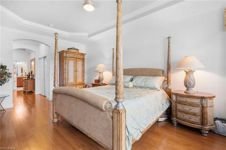 Bedroom featuring arched walkways, crown molding, a closet, wood finished floors, and ensuite bath