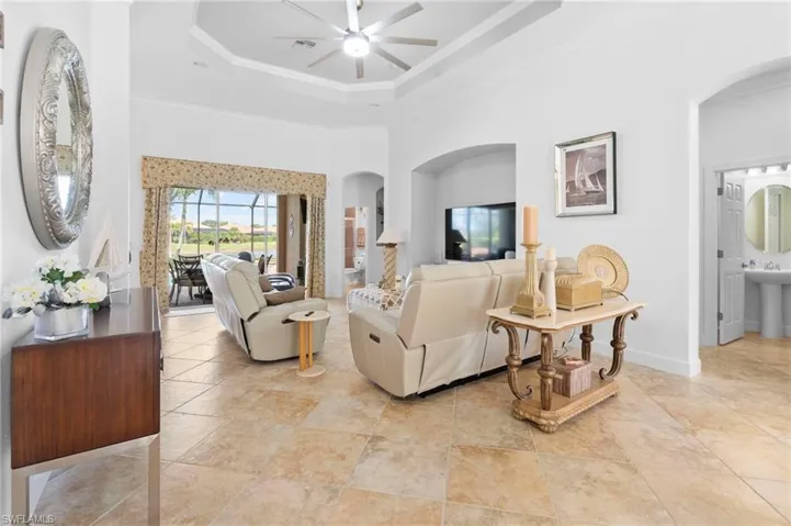 Living area with arched walkways, a high ceiling, a tray ceiling, ornamental molding, and ceiling fan