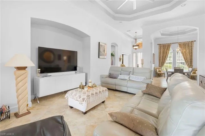 Living area with a tray ceiling, ornamental molding, a towering ceiling, arched walkways, and a ceiling fan