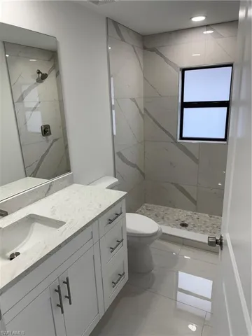 Bathroom with tiled shower, vanity, and toilet