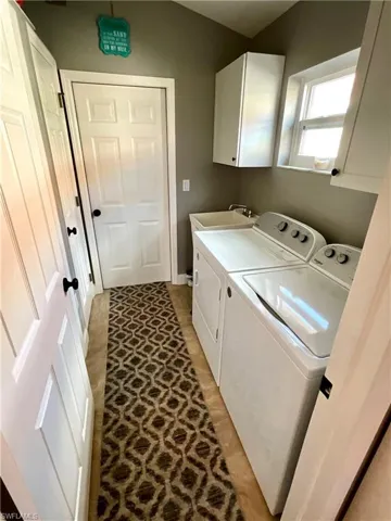 Laundry area with washer and dryer, light tile patterned floors, cabinets, and sink