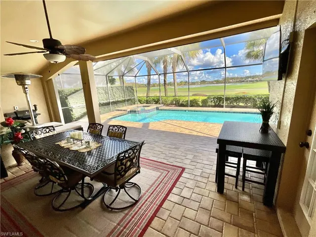 View of swimming pool featuring glass enclosure, ceiling fan, a patio, and an in ground hot tub