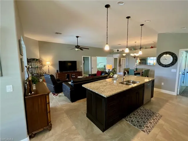 Kitchen featuring light granite counters, ceiling fan with notable chandelier, a kitchen island with sink and pendant lighting
