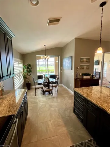 Kitchen featuring vaulted ceiling, electric stove, light stone countertops, and decorative light fixtures