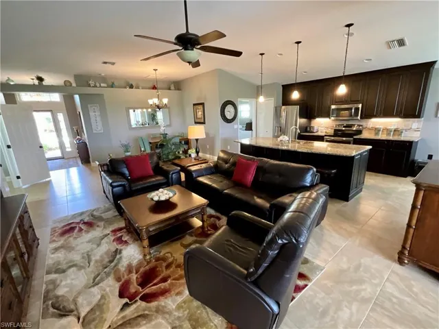 Living room with sink, light tile patterned floors, and ceiling fan with notable chandelier