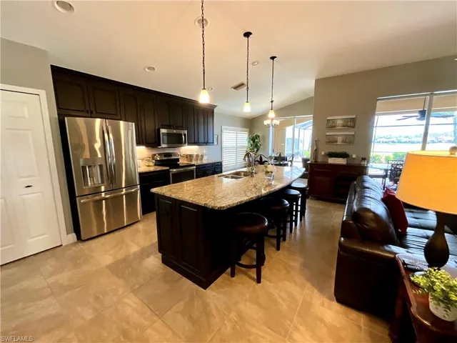 Kitchen with light granite countertops, a kitchen bar, stainless steel appliances, a kitchen island with sink, and hanging light fixtures