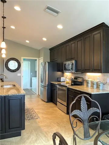 Kitchen featuring light granite countertops, sink, independent washer and dryer, pendant lighting, and appliances with stainless steel finishes