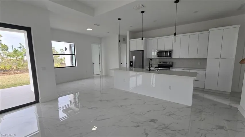 Kitchen with white cabinetry, a kitchen island with sink, stainless steel appliances, hanging light fixtures, and modern cabinets
