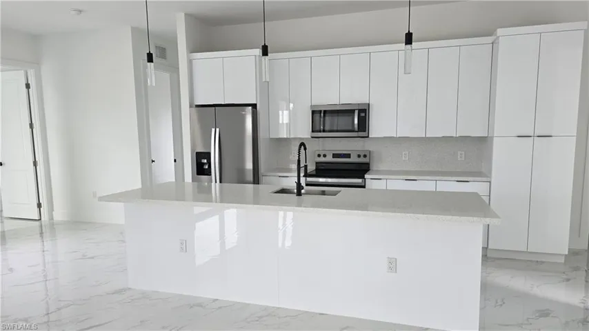 Kitchen with stainless steel appliances, white cabinetry, light stone counters, and decorative backsplash