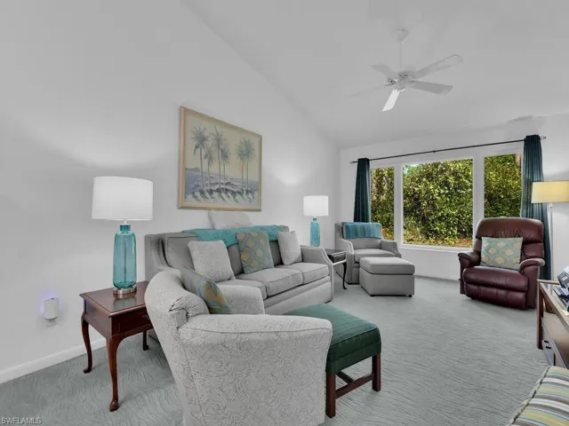 Carpeted living room with ceiling fan and high vaulted ceiling