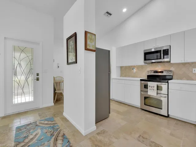Kitchen with tasteful backsplash, white cabinetry, high vaulted ceiling, and appliances with stainless steel finishes