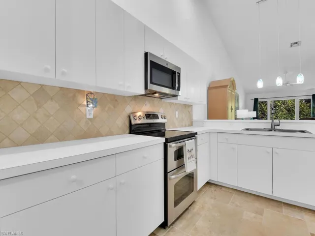Kitchen featuring appliances with stainless steel finishes, vaulted ceiling, sink, white cabinetry, and hanging light fixtures