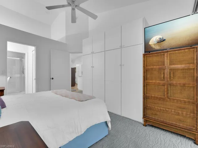 Carpeted bedroom featuring ensuite bath, ceiling fan, a closet, and high vaulted ceiling