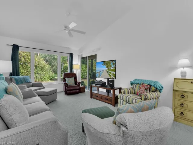 Living room with ceiling fan, light colored carpet, and high vaulted ceiling