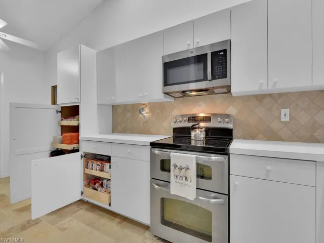 Kitchen featuring decorative backsplash, white cabinetry, stainless steel appliances, and lofted ceiling