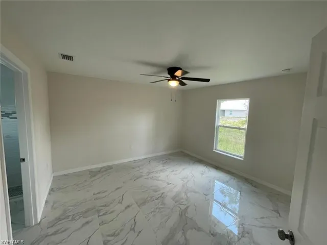 Empty room with light marble finish flooring, baseboards, and a ceiling fan