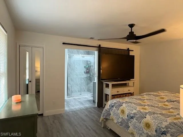 Bedroom featuring a ceiling fan, ensuite bath, wood finished floors, and a barn door