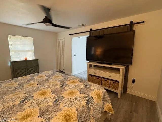 Bedroom with a barn door, dark wood-style flooring, and ceiling fan