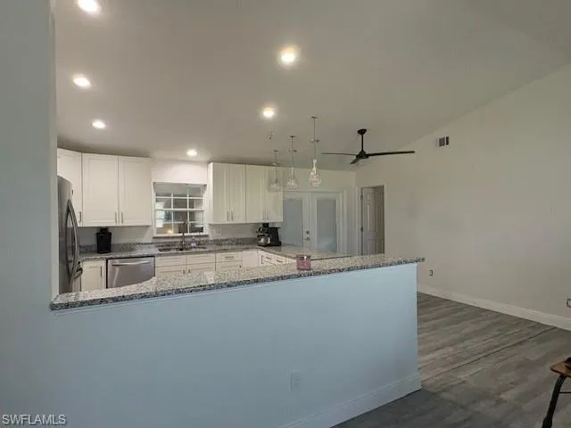 Kitchen with dark stone countertops, white cabinetry, a peninsula, decorative light fixtures, and stainless steel appliances
