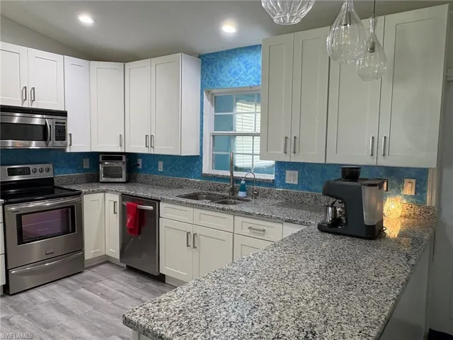 Kitchen with dark stone counters, stainless steel appliances, white cabinets, light wood finished floors, and hanging light fixtures
