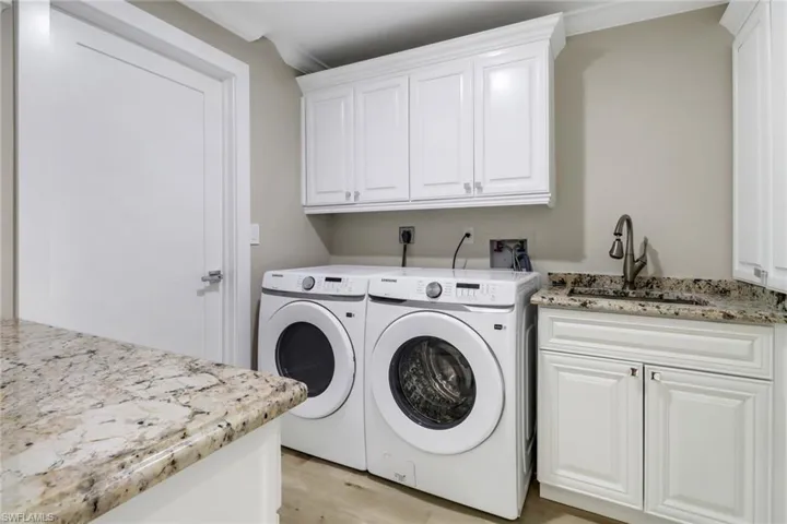 Clothes washing area with sink, cabinets, light hardwood / wood-style floors, independent washer and dryer, and ornamental molding