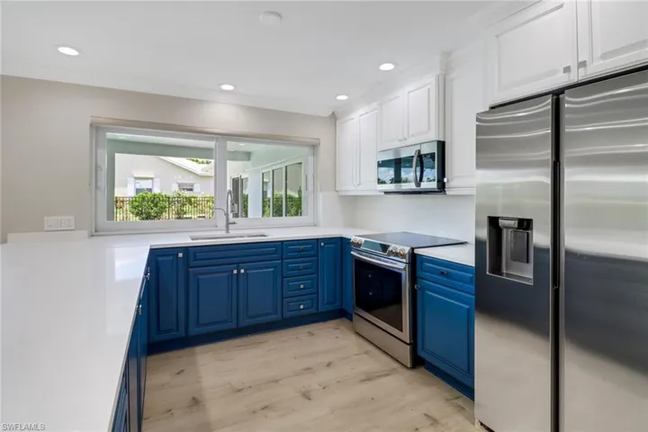 Kitchen featuring stainless steel appliances, sink, light hardwood / wood-style floors, white cabinetry, and blue cabinetry
