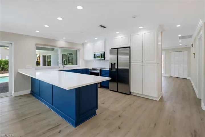 Kitchen with appliances with stainless steel finishes, kitchen peninsula, light hardwood / wood-style flooring, and white cabinets