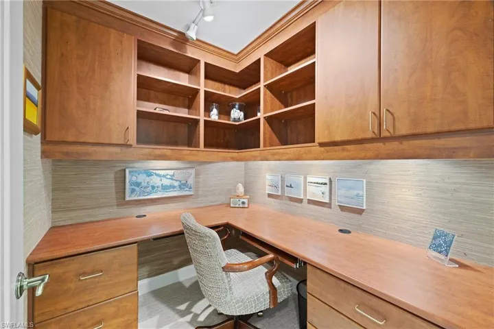 Built-in wood-finish desk with L-shaped configuration, integrated storage cabinetry, and upper shelving