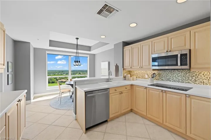 Kitchen featuring light wood cabinetry, stainless steel appliances, mosaic tile backsplash, and light-toned countertops