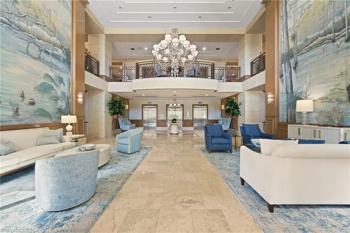 Two-story lobby featuring a grand central chandelier, detailed wall murals, upper-level balcony with decorative railings, and polished tile flooring