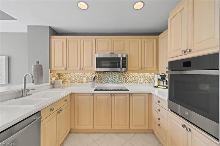 Neutral-toned cabinetry, light-toned countertops, tile flooring, mosaic tile backsplash, and stainless-steel appliances