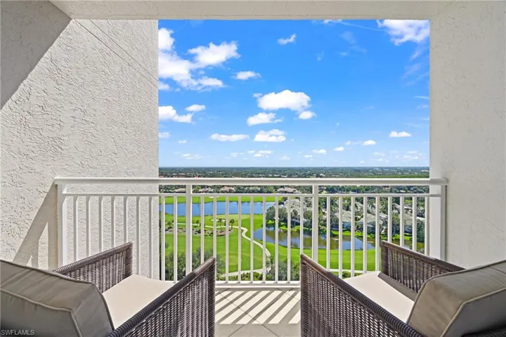 Open-air balcony with white railings, offering an expansive golf course and water feature backdrop