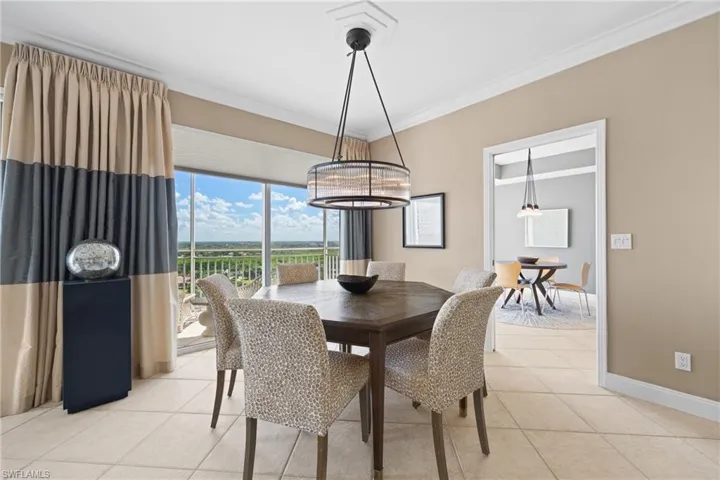 Expansive windows with outdoor scenery, tray ceiling with crown molding, contemporary drum pendant light fixture, tile flooring, and a cased opening to an additional room