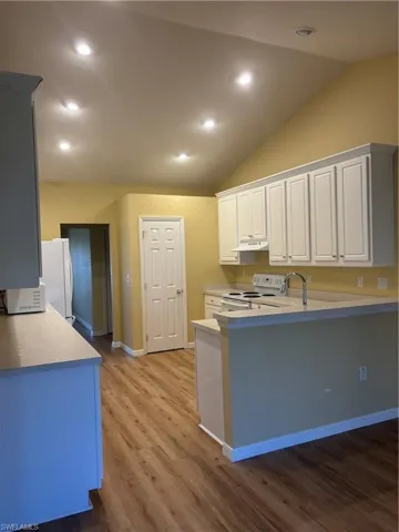 Kitchen featuring white cabinetry, lofted ceiling, kitchen peninsula, and stove