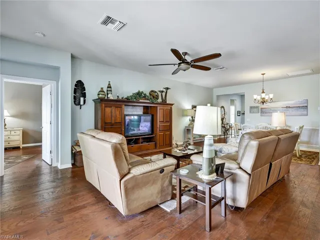 Living room with ceiling fan, suspended lighting, and dark wood-style flooring