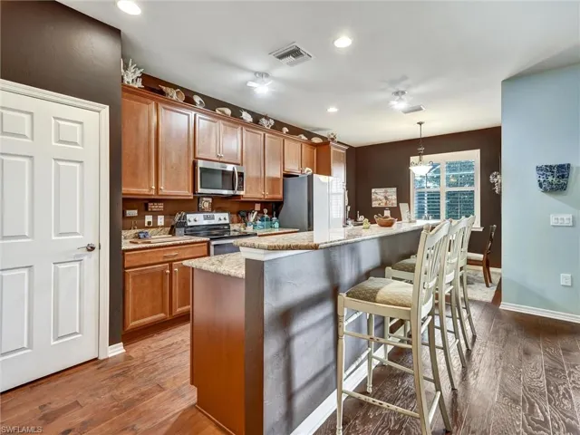 Kitchen featuring hanging light fixtures, stainless steel appliances, a breakfast bar, a center island with sink, and wood finish cabinets