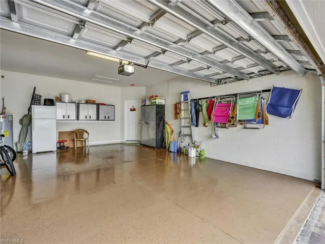 Garage with freestanding refrigerator, concrete block wall, water heater, and a garage door opener