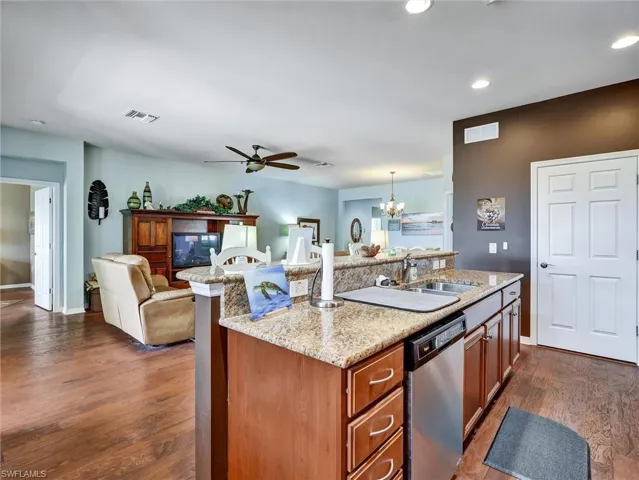 Kitchen with an island with sink, open floor plan, light stone countertops, a chandelier, and dishwasher