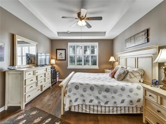 Bedroom with dark wood-type flooring, a tray ceiling, and a ceiling fan