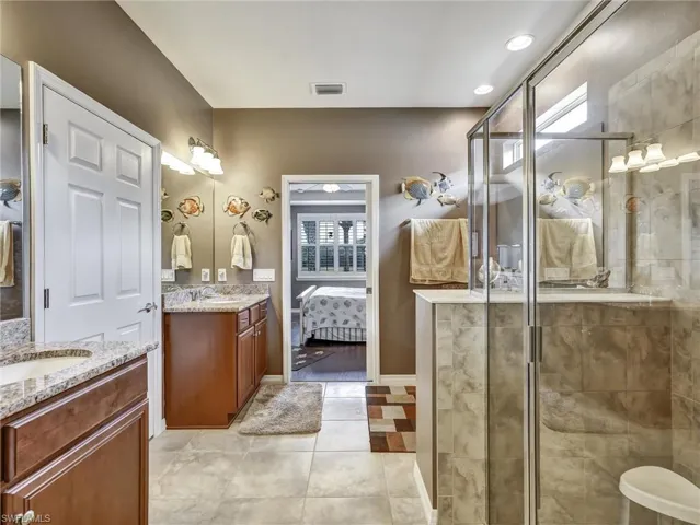 Ensuite bathroom with two vanities, a shower stall, light tile patterned flooring, and recessed lighting
