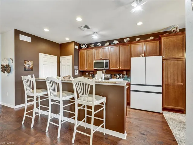 Kitchen featuring freestanding refrigerator, dark wood-type flooring, wood finish cabinets, a breakfast bar, and recessed lighting